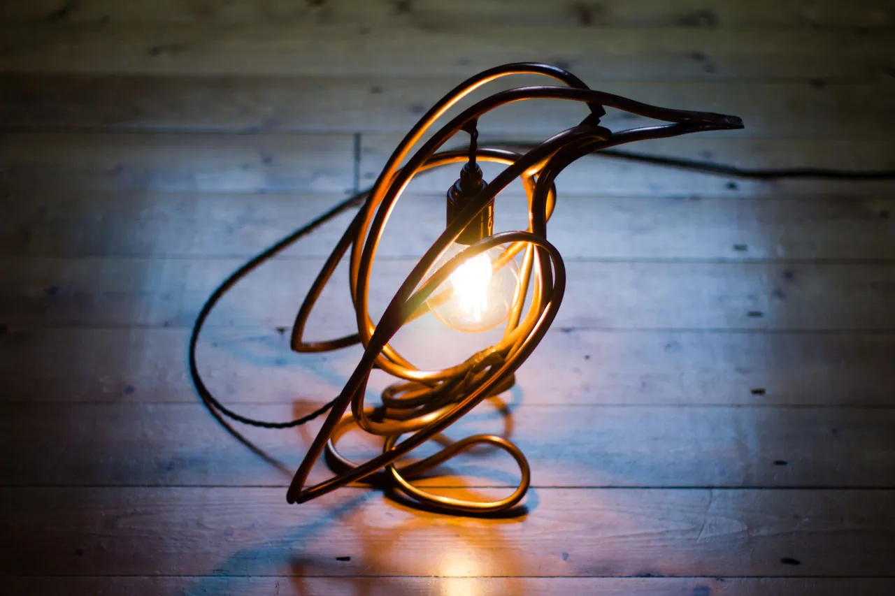 The lit penguin lamp on bare floorboards in a dark room, seen from above with its braided cord trailing behind.