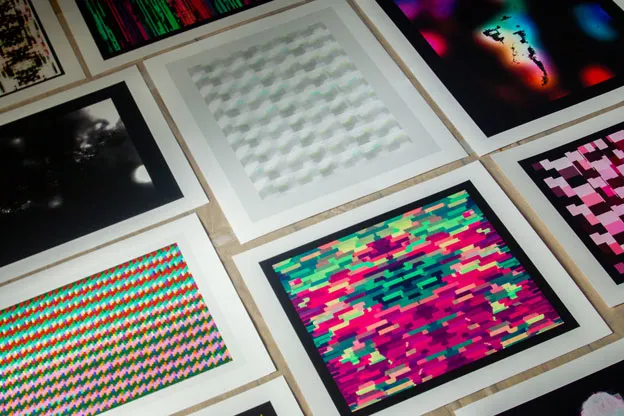 Several glitch prints with white borders laid out at an angle on a wooden surface.