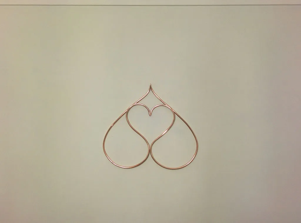 A small double-heart of copper pipe hanging on a pale wall.