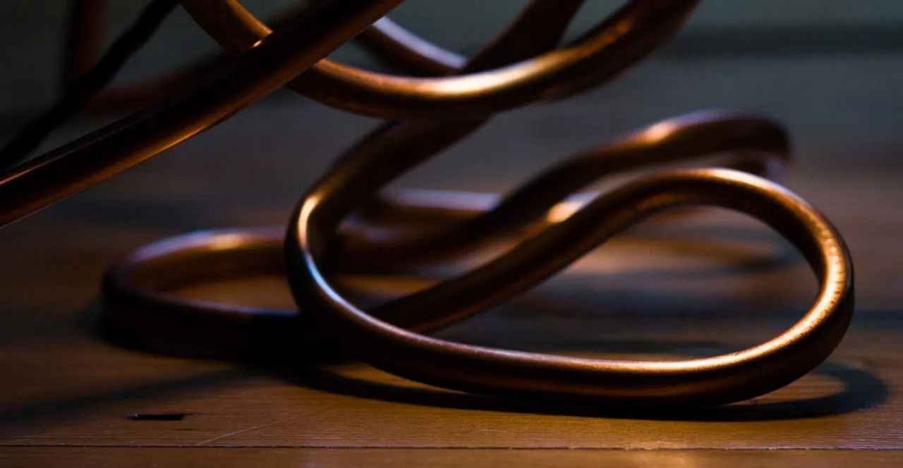 Low close-up of the looped copper feet resting on a wooden floor, with the lower body pipes above them.