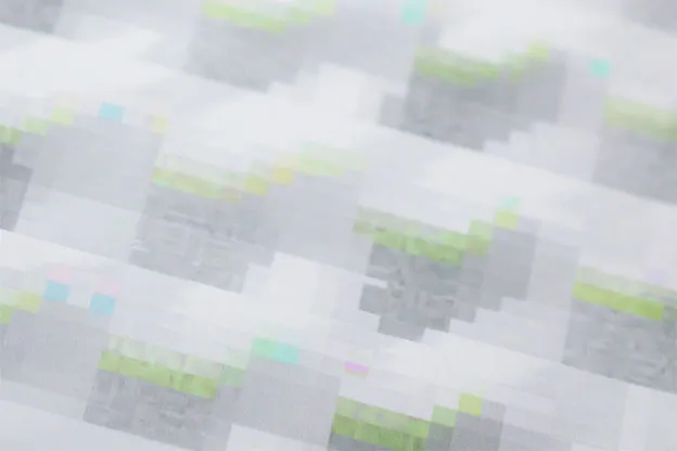 Angled close-up of a pale print with faint grey blocks and touches of lime green and cyan.