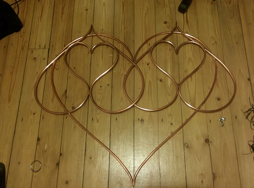 Two double-hearts joined inside one large copper heart, laid out on a wooden floor.