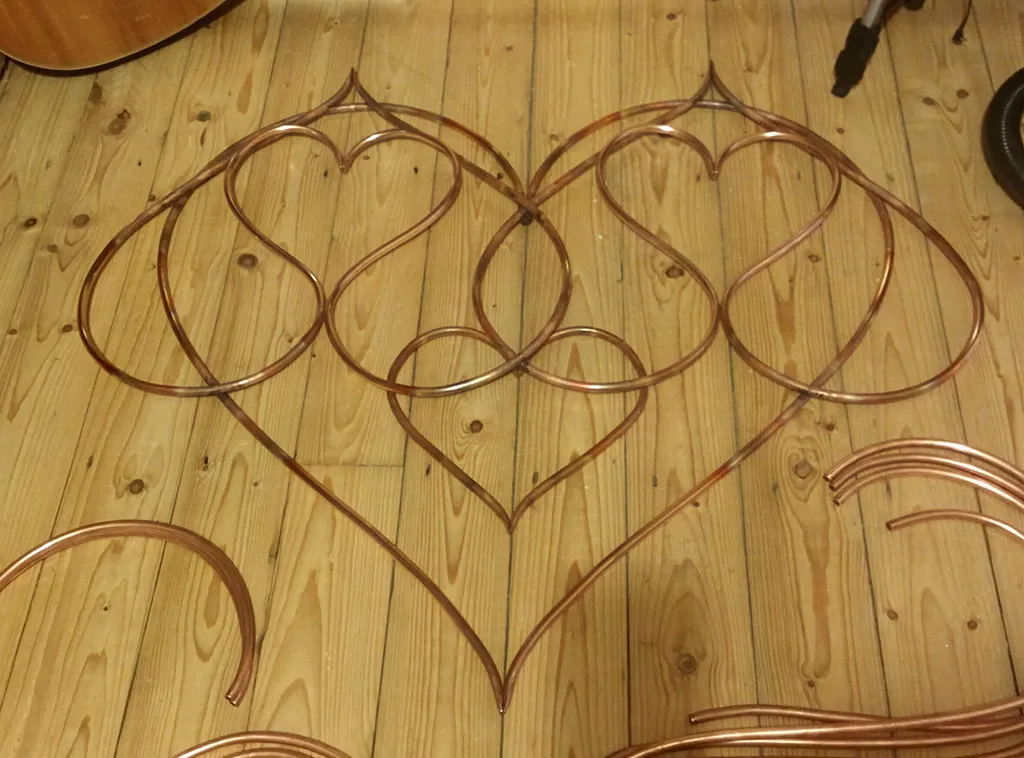 The partly assembled piece on the floor with a small heart added in the middle, discoloured from brazing, and spare pipe lengths around it.
