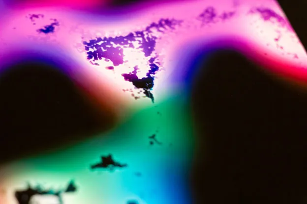Close-up of the corner of a print with glowing pink, blue, and green blurs and dark speckled shapes.