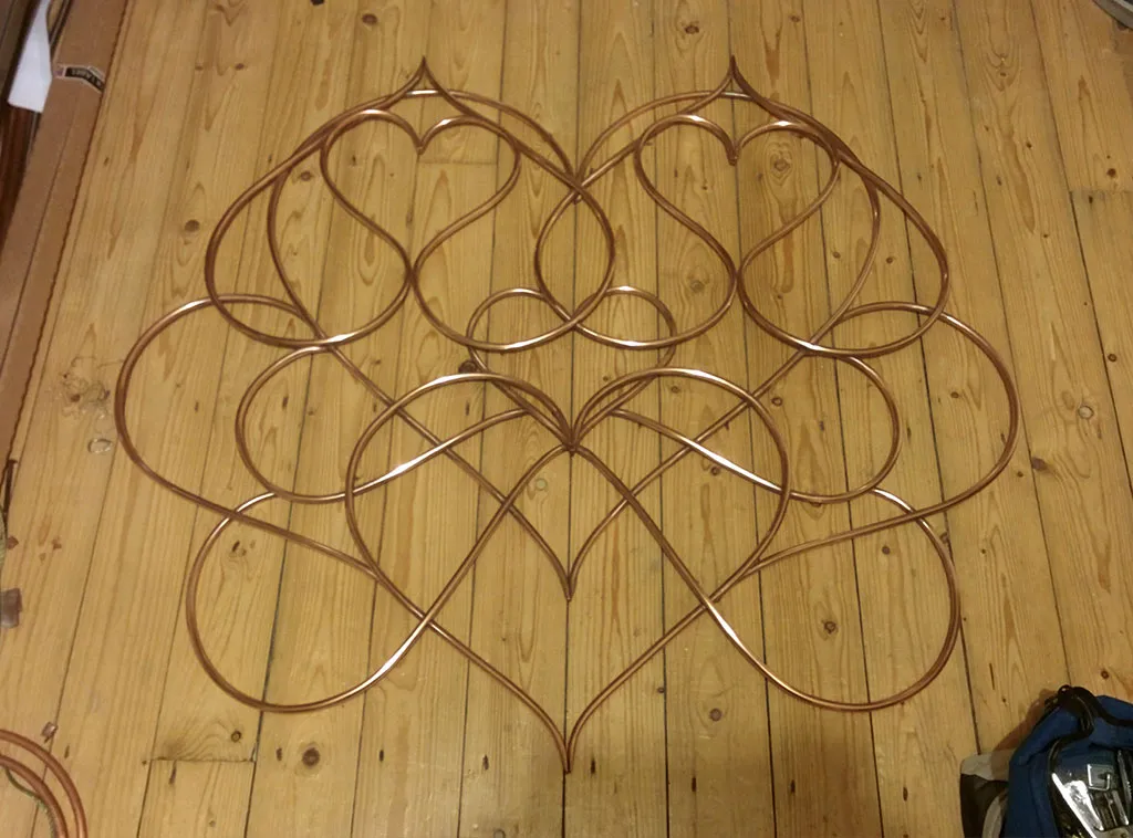 The completed piece, cleaned and shiny, lying flat on a wooden floor.