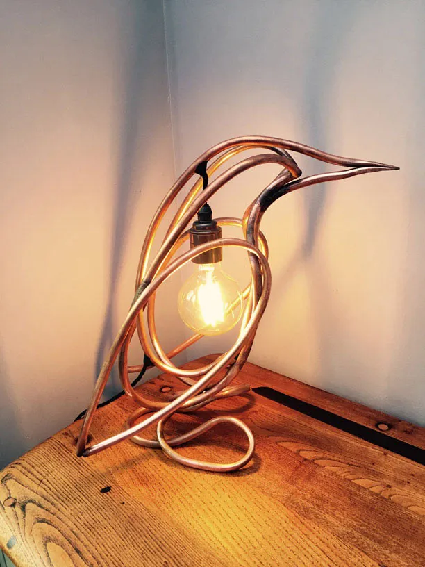 The lit lamp facing right on a wooden chest in the corner of a pale room.