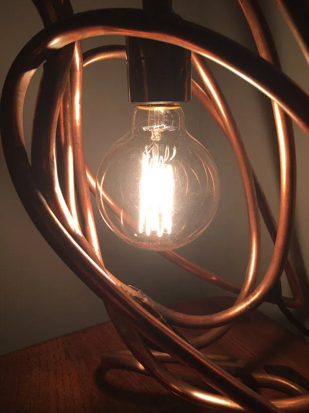 Close-up of the lit bulb inside the polished copper loops.