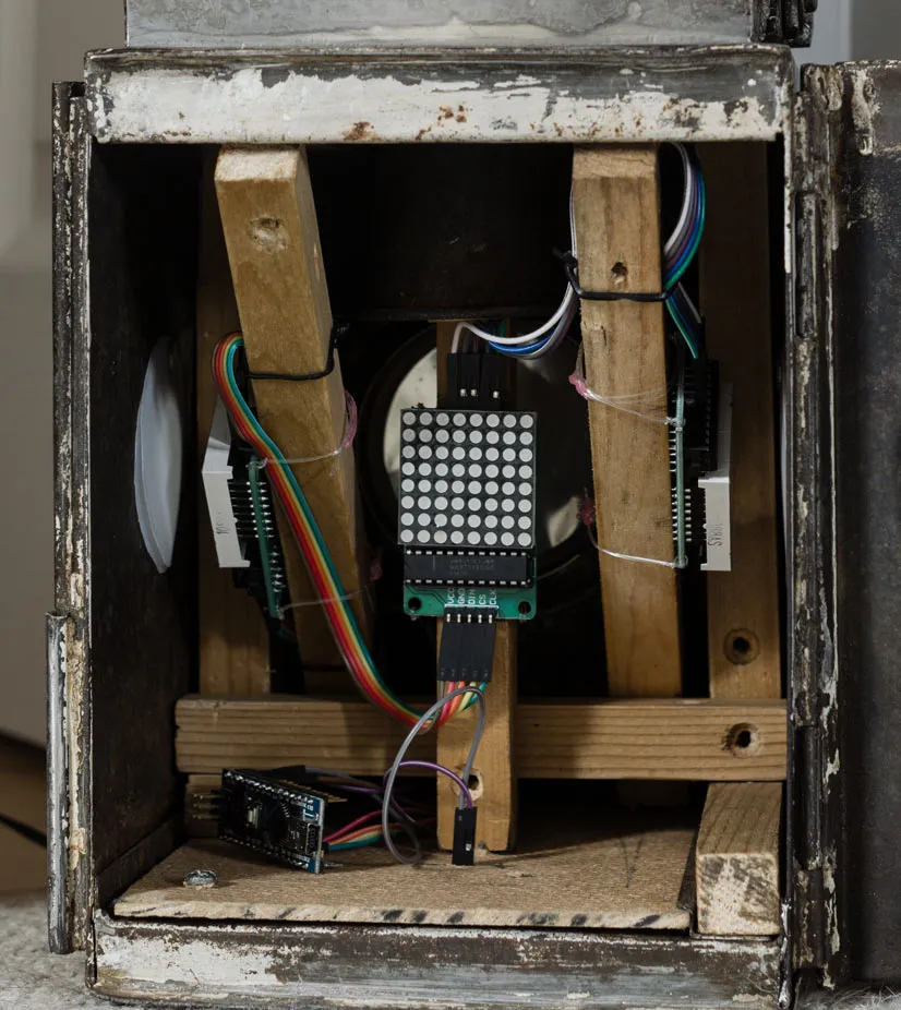 The open lamp body with wooden struts wedged inside, holding LED matrix boards facing the lens and side windows, and an Arduino Nano wired up on the floor.