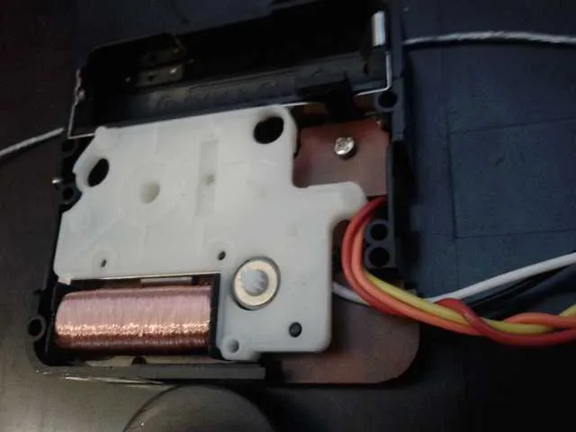 The opened clock movement, showing its white plastic gear housing and copper coil, with a bundle of coloured wires leaving through the side of the case.