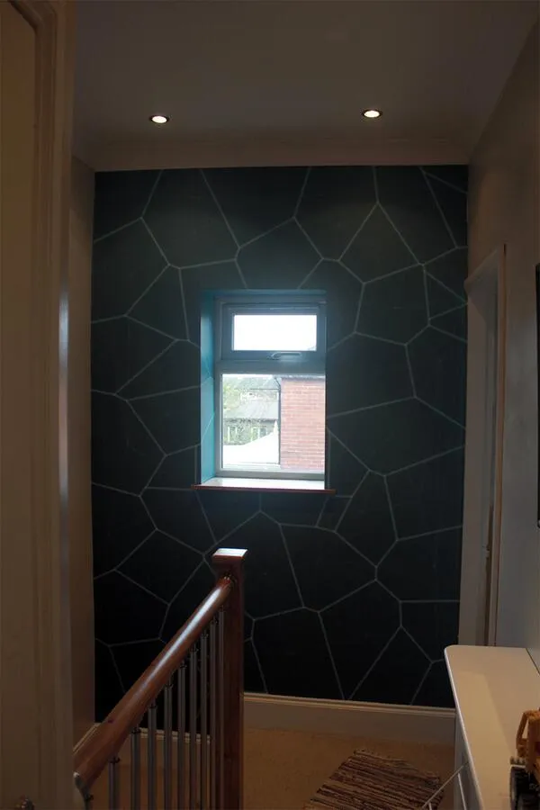 The printed wallpaper on a small dark wall around a window at the top of a staircase.