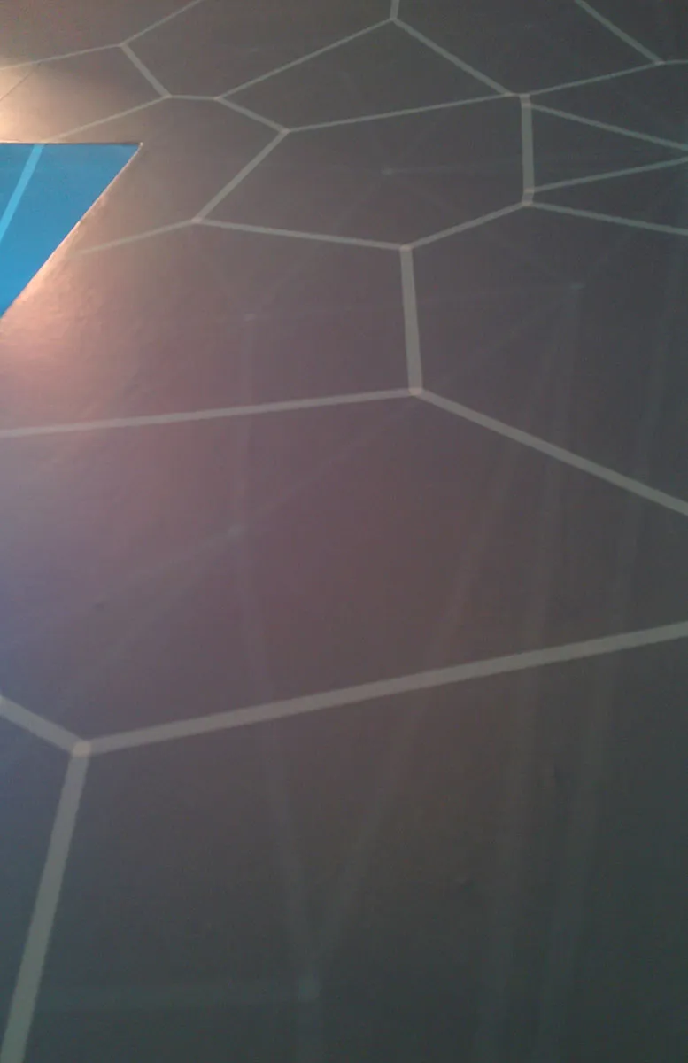 A close-up of the wallpaper's pale cell lines on the dark wall, beside the blue window reveal.