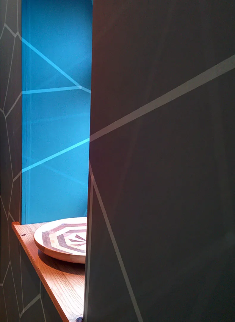 The design continuing onto the blue panel inside the window recess, above a wooden sill with a striped wooden bowl.